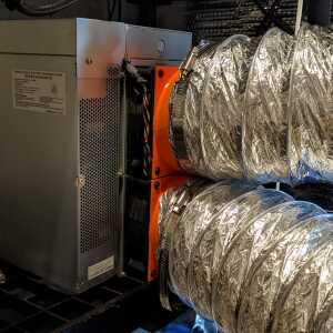 Two silver flexible ducts connected to orange fittings on the side of a metal equipment enclosure.