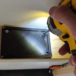 Installing The Tomb hidden seed plate holder base on a wooden surface with four screws