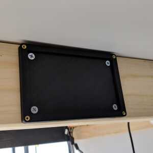 Black The Tomb Bitcoin seed plate holder base fastened to a wooden surface
