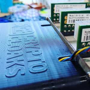 Close-up of raised CryptoCloaks branding on a dark shroud beside circuit boards and colored wires.
