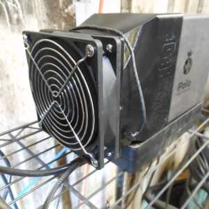 Dark tapered shroud between a square fan with a wire guard and a metal equipment enclosure on a shelf.