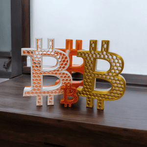 White orange and gold Big Bitcoin B displays shown together on a shelf