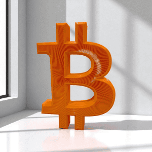 Orange Big Bitcoin B 3D printed desk display standing beside a window