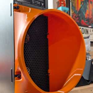 Close-up into an orange circular-mouth shroud attached to silver equipment, with a black honeycomb grille inside.