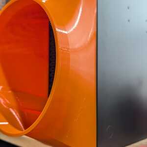 Tight side detail of an orange curved shroud beside a silver enclosure, with a narrow black grille visible inside.