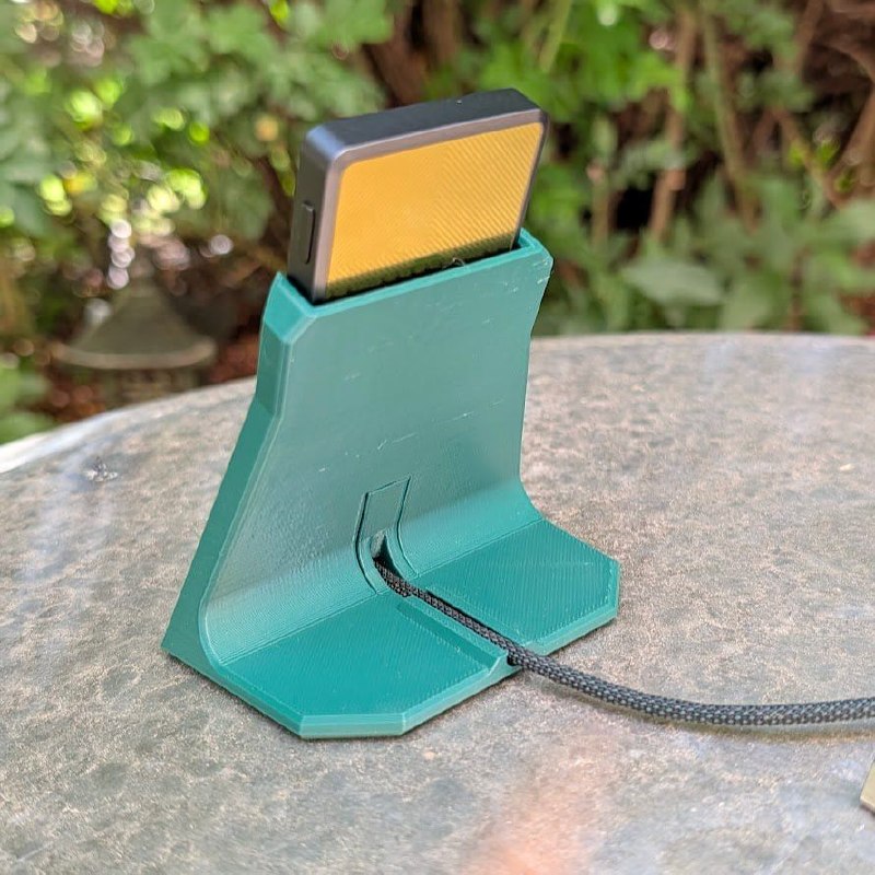 Trezor Safe 7 Dock in teal holding a hardware wallet with USB-C cable on an outdoor table