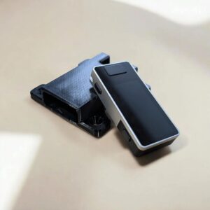 Silver and black Jade Plus hardware wallet beside a black CryptoCloaks mount on a beige surface
