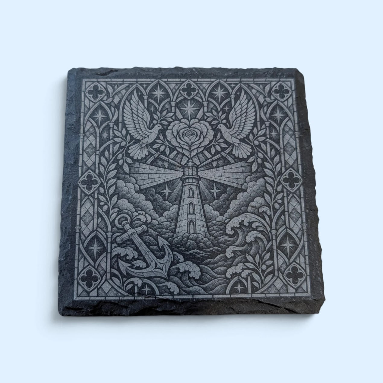 Physical square slate coaster engraved with a lighthouse, anchor, two doves and a heart-shaped rose in a detailed Gothic stained-glass style